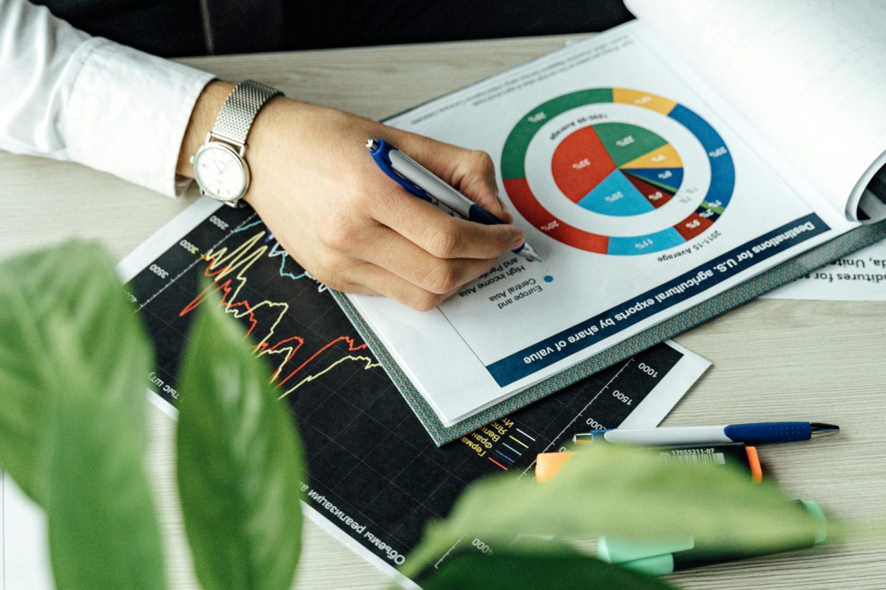 Business professional analyzing financial graphs and charts at an office desk with a laptop.